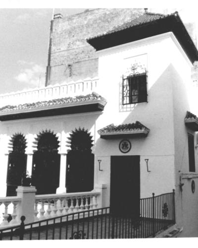 A black and white photograph of a white building featuring Moorish-style horseshoe arches, a tiled roof, and a balcony with a balustrade.