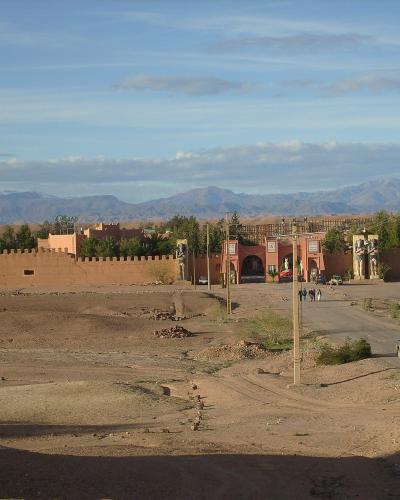 A wide shot of a large, fortified film set entrance with Egyptian-style statues and arches, set against a backdrop of desert terrain and mountains.