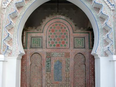 A courtyard with white walls, horseshoe arches, a central fountain, and a distinctive green-tiled roof structure in the background.