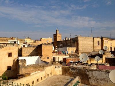 A rooftop view of a dense urban area with beige buildings, a prominent minaret in the background, and several satellite dishes in the foreground.