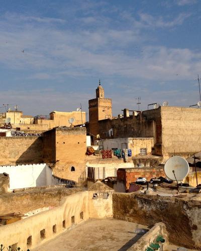 A rooftop view of a dense urban area with beige buildings, a prominent minaret in the background, and several satellite dishes in the foreground.