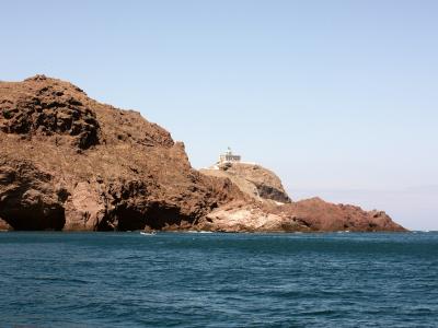 A silhouette of a rugged coastal promontory in the foreground with a boat moving across the sea, illuminated by golden sunset light.