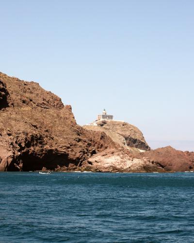 A silhouette of a rugged coastal promontory in the foreground with a boat moving across the sea, illuminated by golden sunset light.