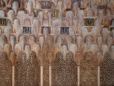 A close-up architectural detail showing intricate stucco muqarnas vaulting and carved wooden lattice screens (mashrabiya) with geometric and floral patterns, typical of Islamic art in Morocco.