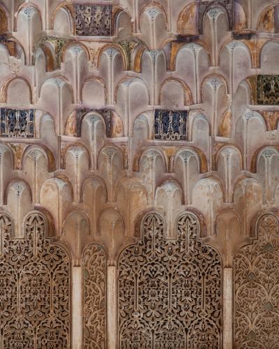 A close-up architectural detail showing intricate stucco muqarnas vaulting and carved wooden lattice screens (mashrabiya) with geometric and floral patterns, typical of Islamic art in Morocco.