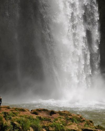 A large waterfall cascading into a pool with two people standing on rocks in the foreground.
