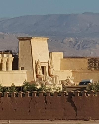 A wide shot of a large, fortified film set entrance with Egyptian-style statues and an arched gateway, set in a desert landscape with mountains in the background.