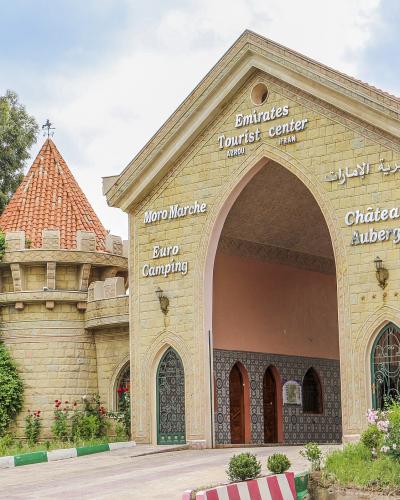 A stone building with an arched entrance and a turret, featuring signage that reads "Emirates Tourist center," "AZROU," "IFRAN," "Moro Marche," "Euro Camping," and "Château Auberge."