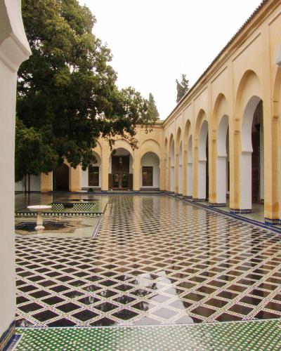 A courtyard with a large reflecting pool, black-and-white diamond-patterned tile flooring, and a colonnade of yellow walls with horseshoe arches.