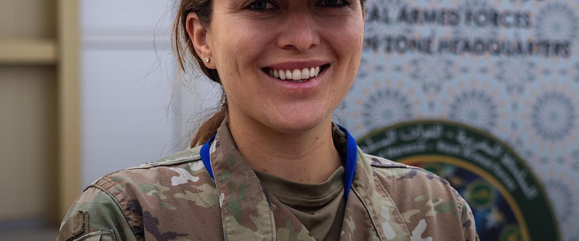 A smiling U.S. Air Force officer in camouflage uniform stands before a banner for "ARCANE THUNDER HIGHLIGHTS" and the "Air Force Culture and Language Center," with Arabic script and partial English text referencing Morocco on the background signage.