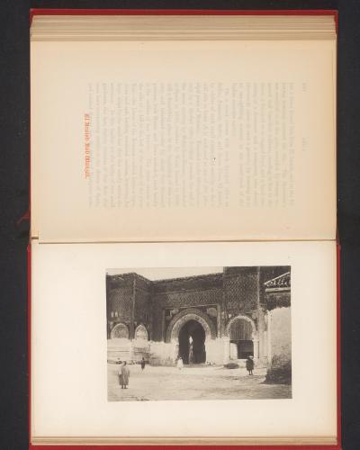 A black and white photograph printed on a page, depicting a large, ornate stone gate with a central archway and decorative tilework above, with several figures in traditional dress standing in the foreground; the page includes printed text and a capt