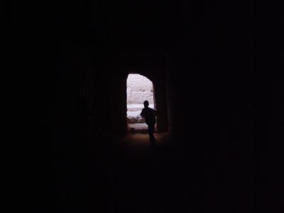 A silhouette of a person standing in a dark, arched doorway looking out toward a bright, textured wall.