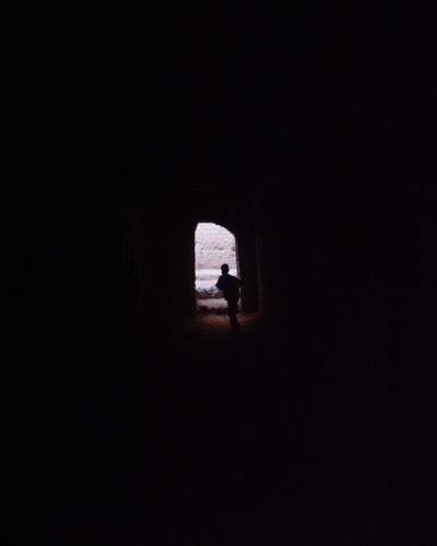 A silhouette of a person standing in a dark, arched doorway looking out toward a bright, textured wall.