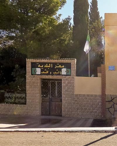 The image shows the entrance gate and facade of a municipal building with a sign reading "مقر البلدية" (Municipal Headquarters) and "سيدي بوزيد للشعب" (Sidi Bouzid for the People), alongside a Moroccan flag.
