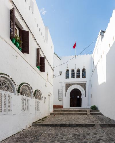 A white-walled courtyard with Moorish-style arched doorways, decorative tilework, and a Moroccan flag flying above the entrance to a building labeled "MUSÉE DE LA KASBAH".