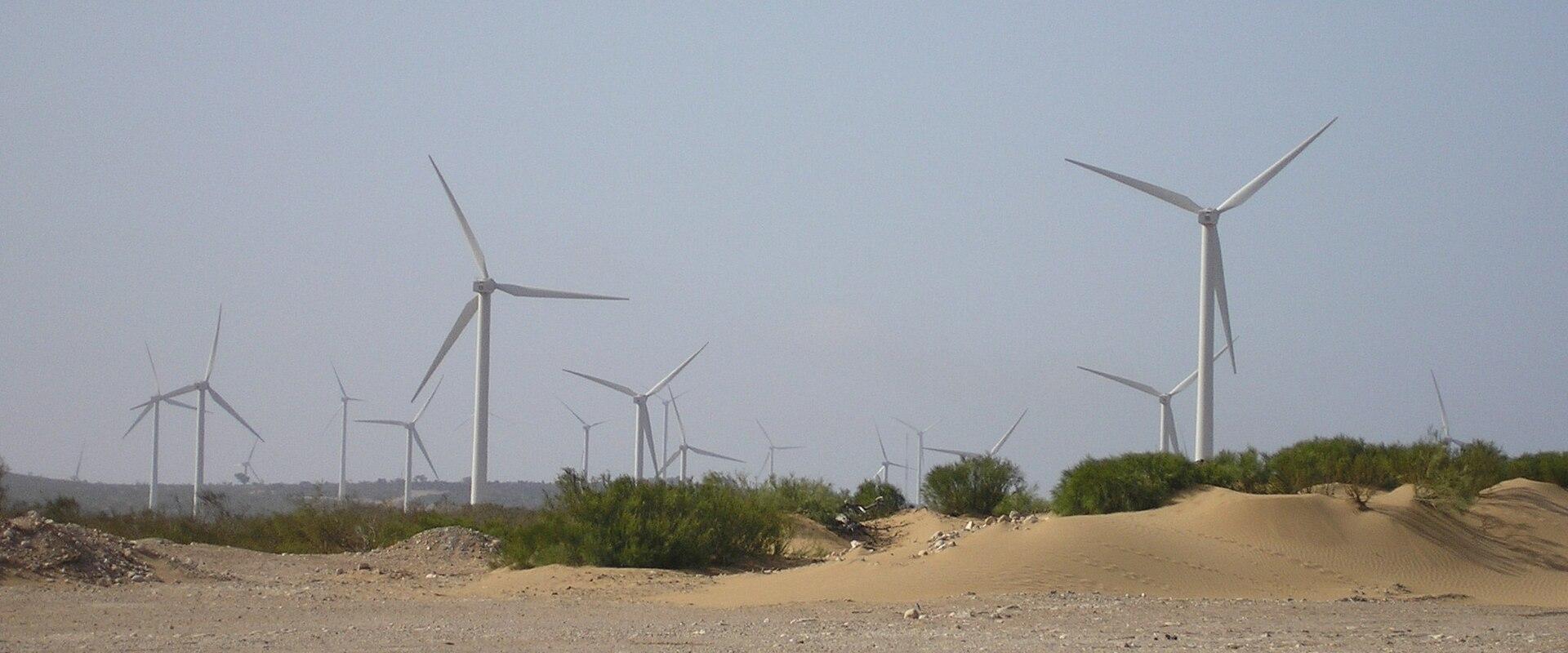 A landscape view of multiple white wind turbines situated on sandy dunes and arid terrain under a hazy sky.