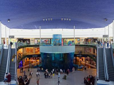 The image shows the interior atrium of a large shopping mall featuring a massive cylindrical aquarium in the center, surrounded by multiple levels of walkways and escalators, with a dark blue ceiling dotted with fiber optic lights resembling a starry